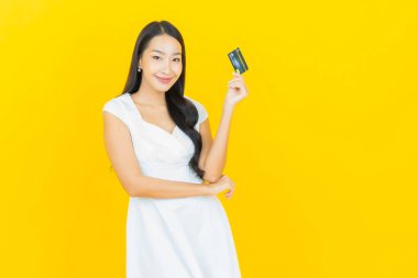 Asyalı güzel bir kadının portresi. Sarı arka planda kredi kartıyla gülümsüyor.