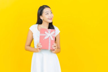 Asyalı güzel bir kadının portresi. Sarı arka planda kırmızı hediye kutusuyla gülümsüyor.