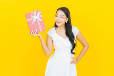 Asyalı güzel bir kadının portresi. Sarı arka planda kırmızı hediye kutusuyla gülümsüyor.