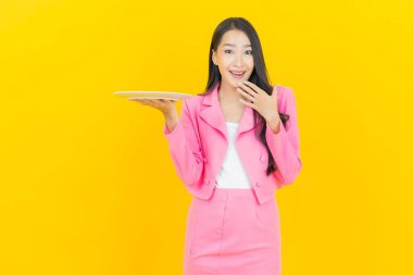 Asyalı güzel bir kadının portresi. Sarı arka planda boş tabak tabağıyla gülümsüyor.