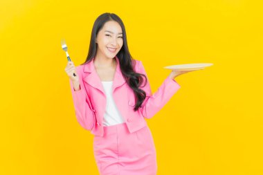 Asyalı güzel bir kadının portresi. Sarı arka planda boş tabak tabağıyla gülümsüyor.