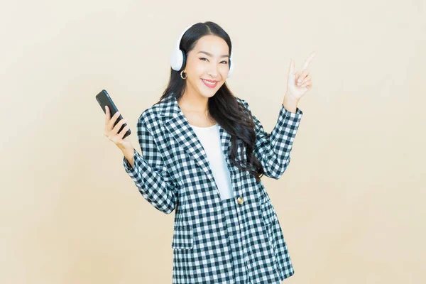 ポートレート美しいです若いですアジアの女性とともにヘッドフォンとスマートフォンのために音楽を聴く黄色の背景 — ストック写真