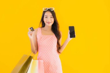 Renkli alışveriş çantalı güzel Asyalı kadın akıllı cep telefonu ve sarı izole edilmiş arka planda kredi kartı.