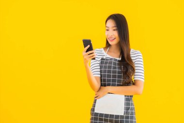 Güzel bir Asyalı kadın portresi sarı izole edilmiş arka planda akıllı cep telefonu kullanıyor.