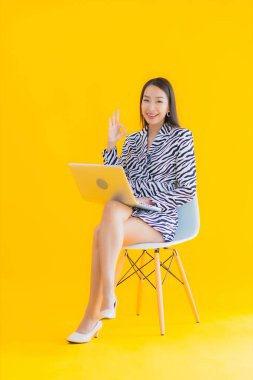 Güzel bir Asyalı kadın, sarı izole edilmiş arka planda dizüstü bilgisayar kullanıyor.