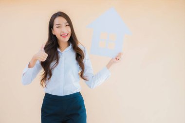 Güzel Asyalı iş kadını portresi izole edilmiş arkaplanda ev işareti ve afişi gösteriyor.