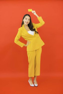 Güzel bir Asyalı kadının portresi kırmızı arka planda kredi kartıyla cep telefonu kullanıyor.