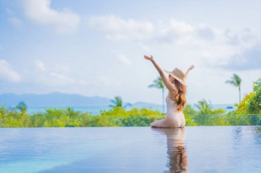 Güzel bir Asyalı kadın portresi gezide deniz manzaralı açık havuzda yüzüyor.