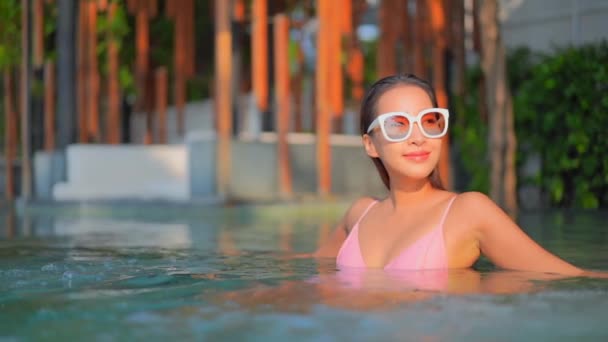 美しい若いアジアの女性の映像休日の休暇のために海のビーチの海の近くの屋外スイミングプールの周りの笑顔のレジャーをリラックス — ストック動画