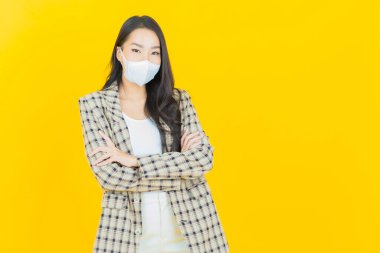 Sarı arka planda Covid19 veya virüsü korumak için maskeli güzel Asyalı kadın portresi