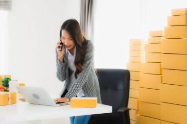 Güzel Asyalı iş kadını portresi evden bilgisayarlı cep telefonuyla karton kutuyla çevrimiçi alışveriş için hazır bekliyor.