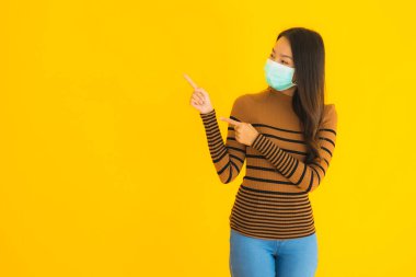 Koronavirüsten korunmak için maske takmış güzel bir Asyalı kadın portresi. Ya da sarı izole edilmiş arka planda kovid19.