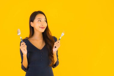 Güzel, genç Asyalı bir kadının portresi. Kaşığı ve çatalı ile sarı izole edilmiş arka planda yemeye hazır.