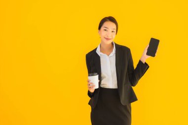 Portre güzel genç Asyalı kadın akıllı cep telefonu ve kahve fincanı ile izole edilmiş sarı arka planda