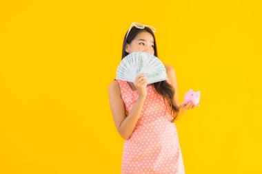 Bir sürü parası ve parası olan güzel Asyalı bir kadının portresi, izole edilmiş sarı arka planda domuz kumbarasıyla.