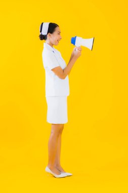 Asyalı güzel bir kadının portresi klinikte ve hastanede iletişim kurmak için megafonlu Taylandlı hemşire ve sarı izole bir arka plan.