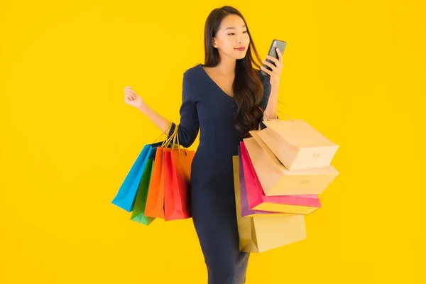 具有购物袋信用卡和智能手机黄色背景的漂亮年轻亚洲女人的肖像 — 图库照片