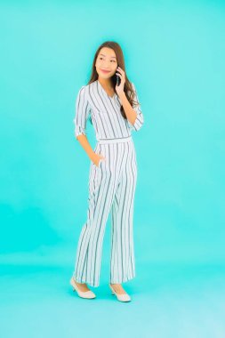 Güzel bir Asyalı kadın portresi mavi arka planda akıllı cep telefonu kullanıyor.