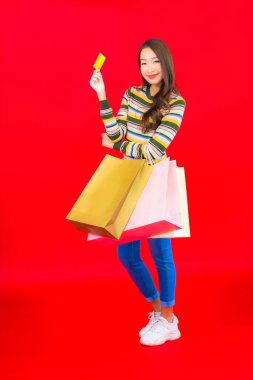 Renkli alışveriş çantası ve kırmızı arka planda kredi kartıyla güzel bir Asyalı kadın portresi