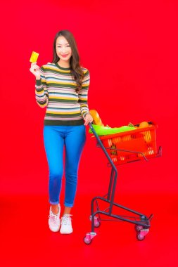 Marketten aldığı alışveriş sepetiyle kırmızı izole arka planda güzel bir Asyalı kadın portresi.