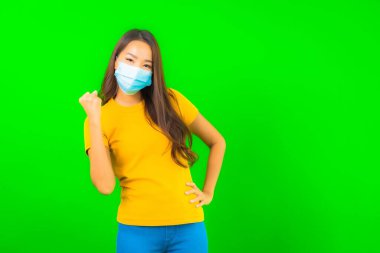 Güzel Asyalı genç bir kadının portresi, yeşil yalıtılmış arka planda kovid19 veya koronavirüsten korunmak için maske takar.