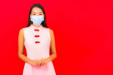 Güzel Asyalı bir kadının portresi, kırmızı izole edilmiş arka planda Covid19 ve Coronavirus 'tan korunmak için maske takar.