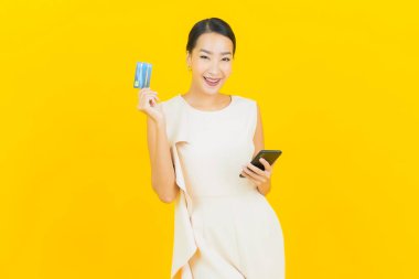 Asyalı güzel bir kadının portresi. Sarı arka planda kredi kartıyla gülümsüyor.