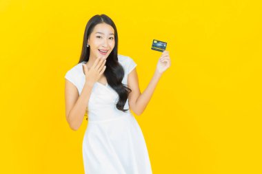 Asyalı güzel bir kadının portresi. Sarı arka planda kredi kartıyla gülümsüyor.