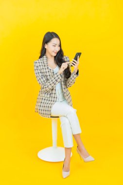 Renkli arka planda akıllı cep telefonuyla güzel Asyalı kadın gülümsemesi