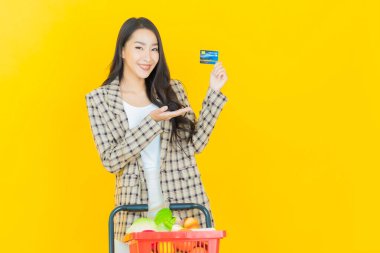 Renkli arka planda süpermarketten alınmış market sepetiyle gülümseyen güzel Asyalı kadın portresi.