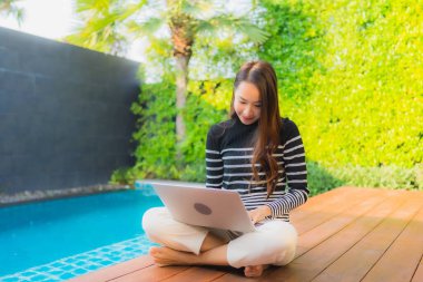 Genç Asyalı bir kadının portresi oteldeki yüzme havuzunda dizüstü bilgisayar kullanıyor.