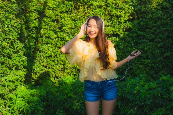 年轻的亚洲女人使用智能手机和耳机聆听户外花园自然景观的音乐 — 图库照片