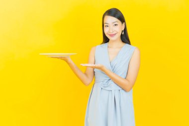 Güzel Asyalı bir kadının portresi. Arka planda boş tabak tabağıyla gülümsüyor.