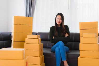 Güzel bir Asyalı kadın portresi evde çalışıyor ve karton kutuları çevrimiçi nakliyeye hazır hale getiriyor.