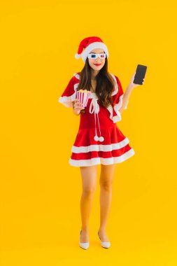 Güzel bir Asyalı kadın portresi patlamış mısır ve 3D gözlüklü noel şapkası takıyor sarı izole edilmiş arka planda film izlemeye hazır.