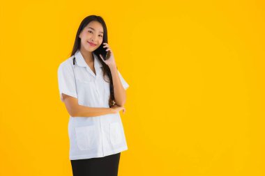 Güzel Asyalı genç doktor kadın sarı izole edilmiş arka planda akıllı cep telefonu kullanıyor.