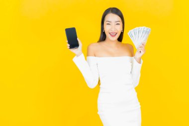 Bir sürü parası ve sarı arka planda kumbarası olan Asyalı güzel bir iş kadını portresi.