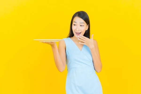 肖像画美しい若いアジアの女性の笑顔とともに空のプレート料理上の黄色の背景 — ストック写真
