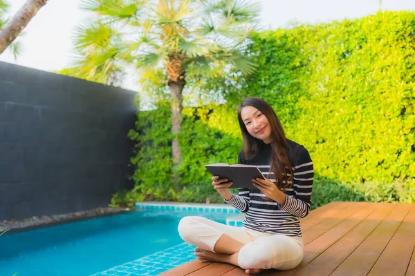 在酒店度假胜地的室外游泳池边 年轻的亚洲女子正在看书 — 图库照片