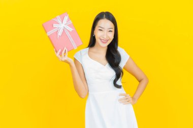 Asyalı güzel bir kadının portresi. Sarı arka planda kırmızı hediye kutusuyla gülümsüyor.