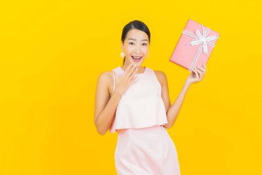 Asyalı güzel bir kadının portresi. Sarı arka planda kırmızı hediye kutusuyla gülümsüyor.