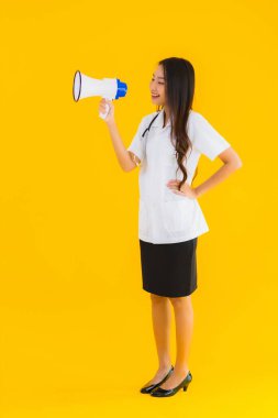 Güzel bir Asyalı genç doktor portresi. Sarı izole arka planda megafon kullanıyor.