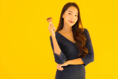 Sarı izole arkaplanda makyaj fırçası olan güzel bir Asyalı kadın portresi.