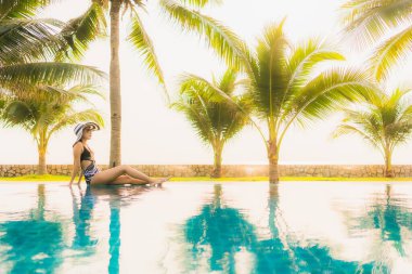 Güzel bir Asyalı kadın portresi, gün batımında palmiye ağacıyla birlikte havuz kenarında dinleniyor ya da tatil için gün doğumunda dinleniyor.
