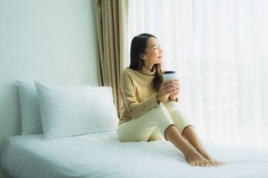 Yatak odasının iç tarafında, kahve fincanı olan Asyalı genç bir kadın.
