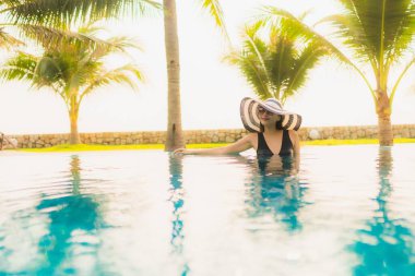 Güzel bir Asyalı kadın portresi, gün batımında palmiye ağacıyla birlikte havuz kenarında dinleniyor ya da tatil için gün doğumunda dinleniyor.