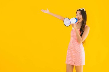 Güzel bir Asyalı kadın, sarı izole edilmiş arka planda megafonla yüksek sesle konuşur.