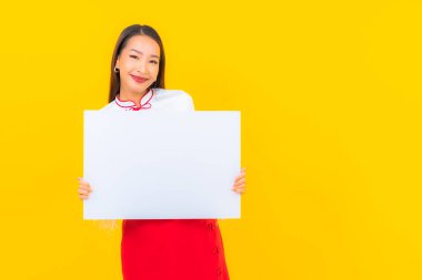Güzel bir Asyalı kadın portresi sarı izole arkaplanda beyaz boş ilan panosu gösteriyor.