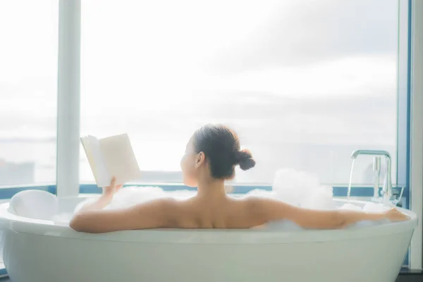 肖像画美しい若いアジアの女性は バスルームのインテリアで白い浴槽で本を読みます — ストック写真