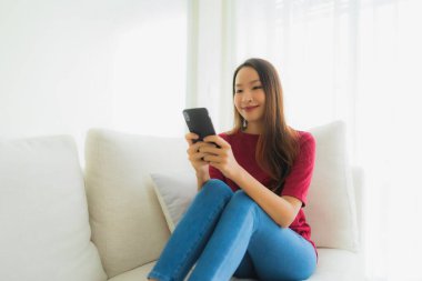 Oturma odasındaki koltukta cep telefonu ya da akıllı telefon kullanan güzel Asyalı kadınların portresi.
